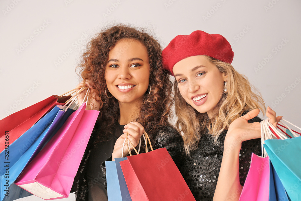 Beautiful young women with shopping bags on light background