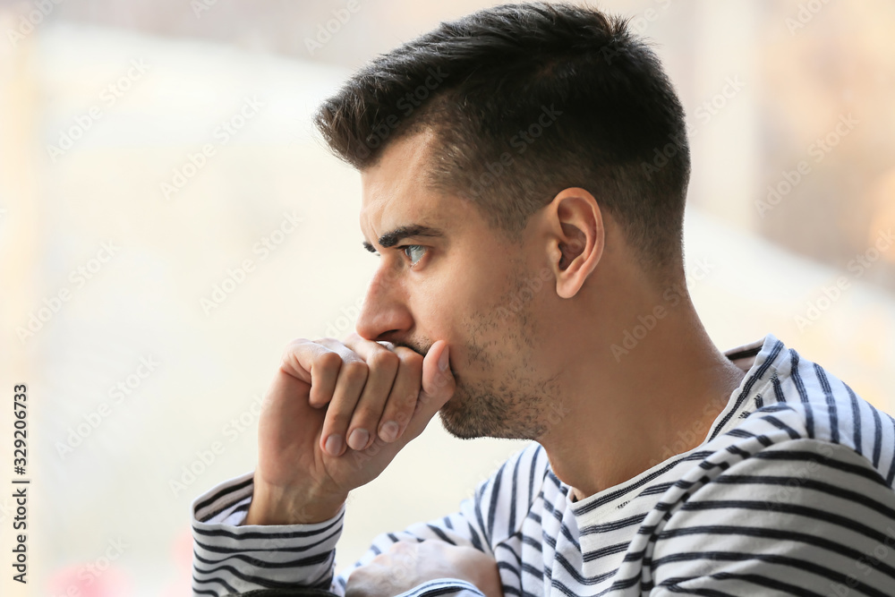 Depressed young man near window at home