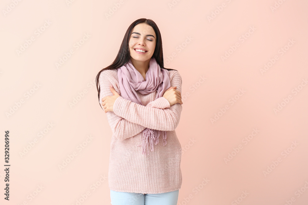 Beautiful young woman in warm sweater on color background