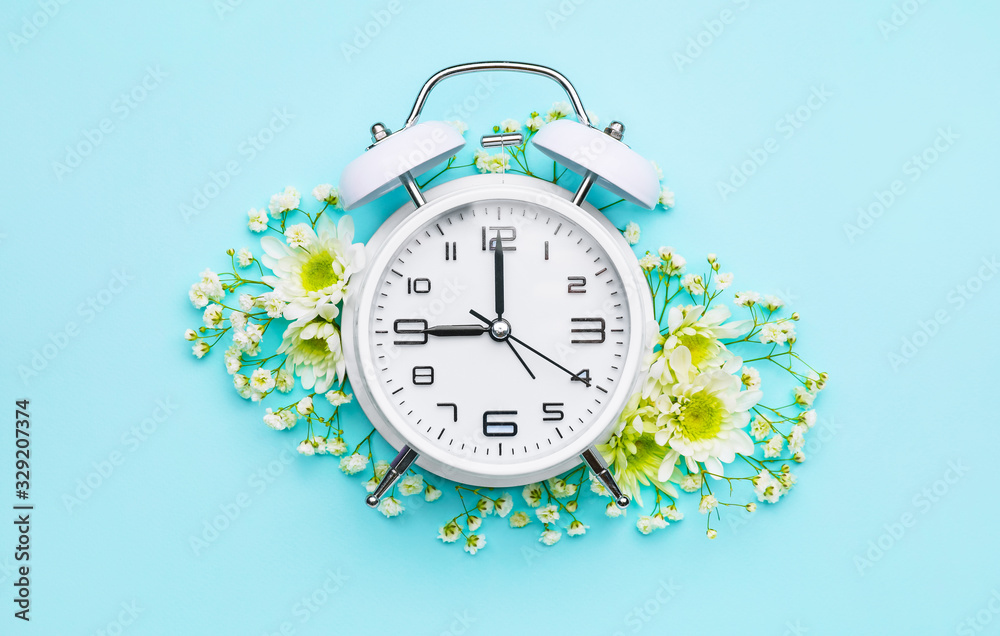 Alarm clock with flowers on color background