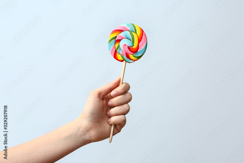 Female hand with sweet lollipop on light background