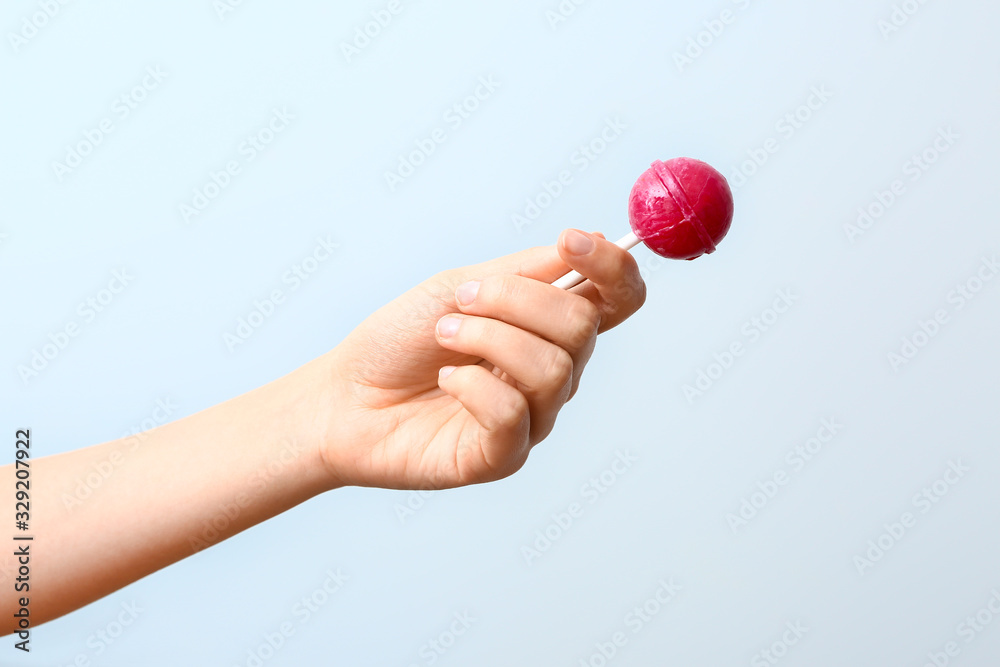 Female hand with sweet lollipop on light background