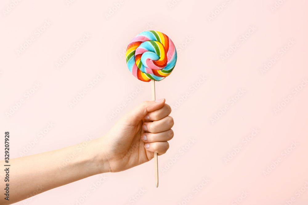 Female hand with sweet lollipop on color background