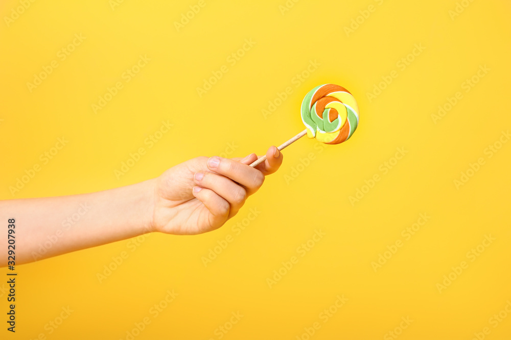 Female hand with sweet lollipop on color background