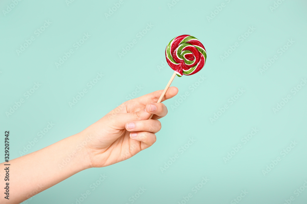 Female hand with sweet lollipop on color background