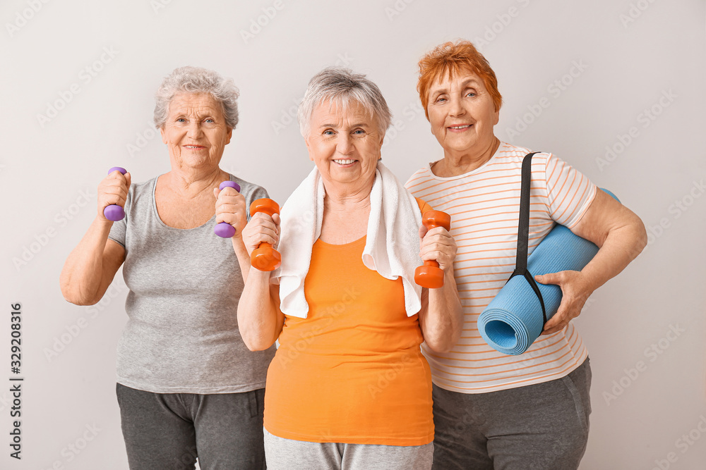 Elderly women with sports equipment on light background