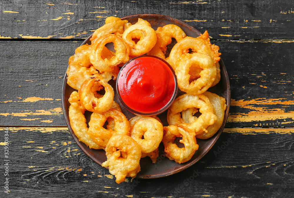 Plate with crispy fried onion rings and sauce on table