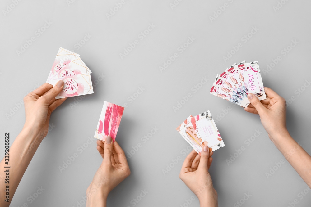 Female hands with business cards of makeup artist on grey background