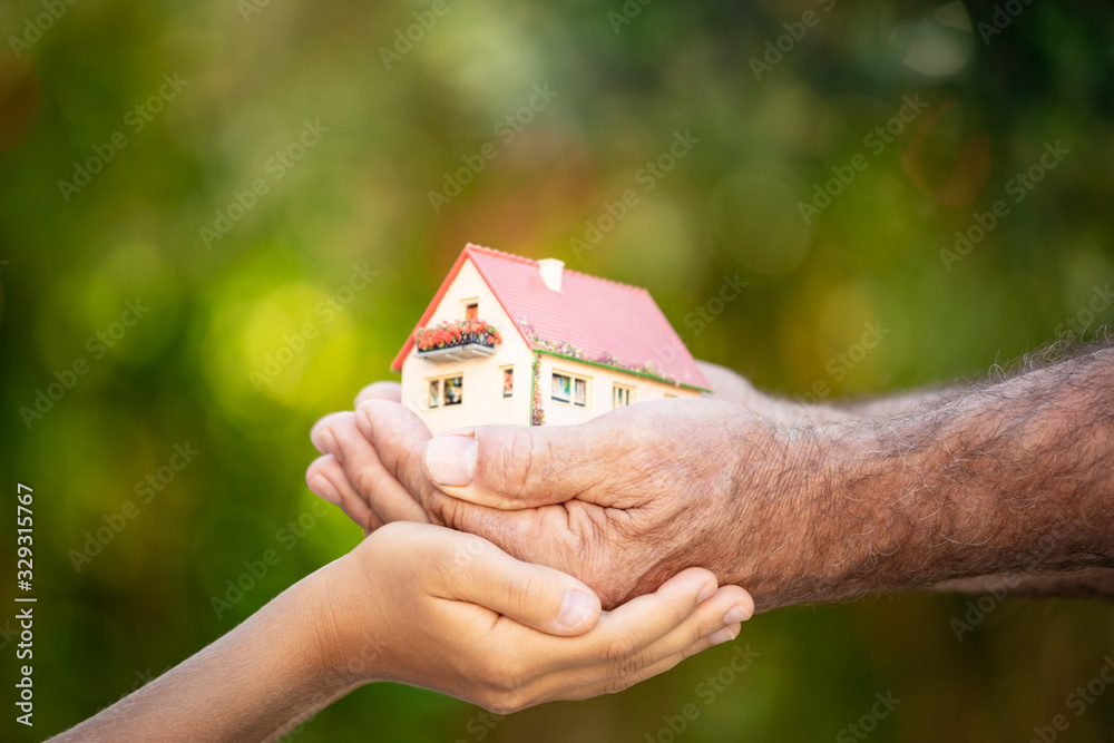 Senior man and child holding house in hands against spring green background