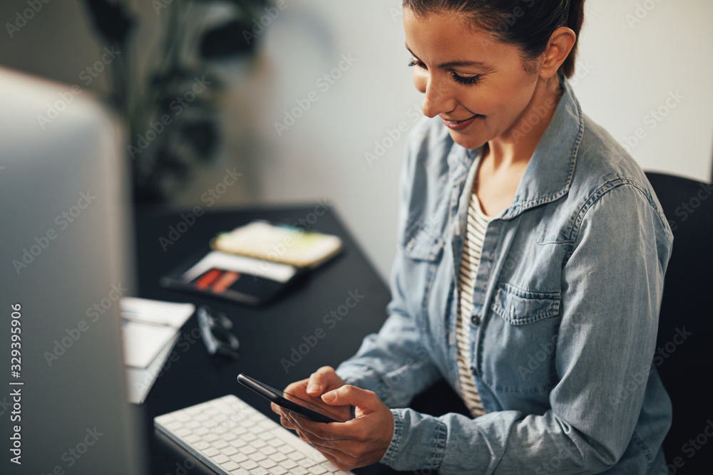 Smiling young businesswoman texting on her cellphone at her desk