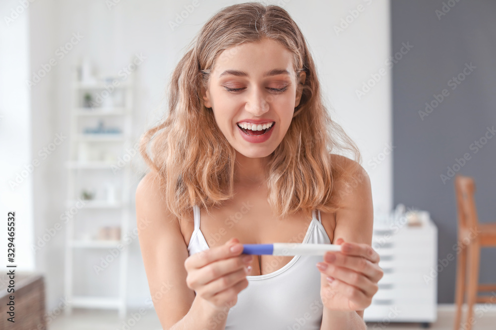 Happy young woman with pregnancy test in bathroom