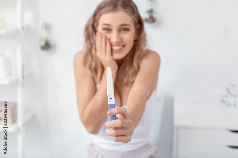 Happy young woman with pregnancy test in restroom