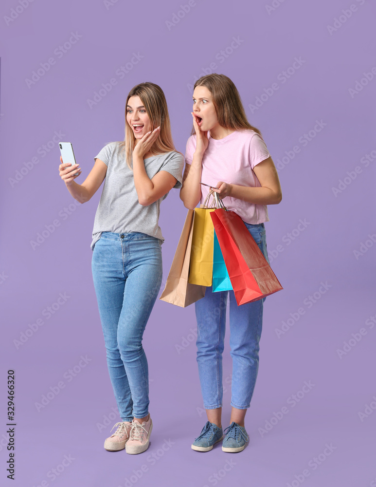 Surprised young women with mobile phone and shopping bags on color background