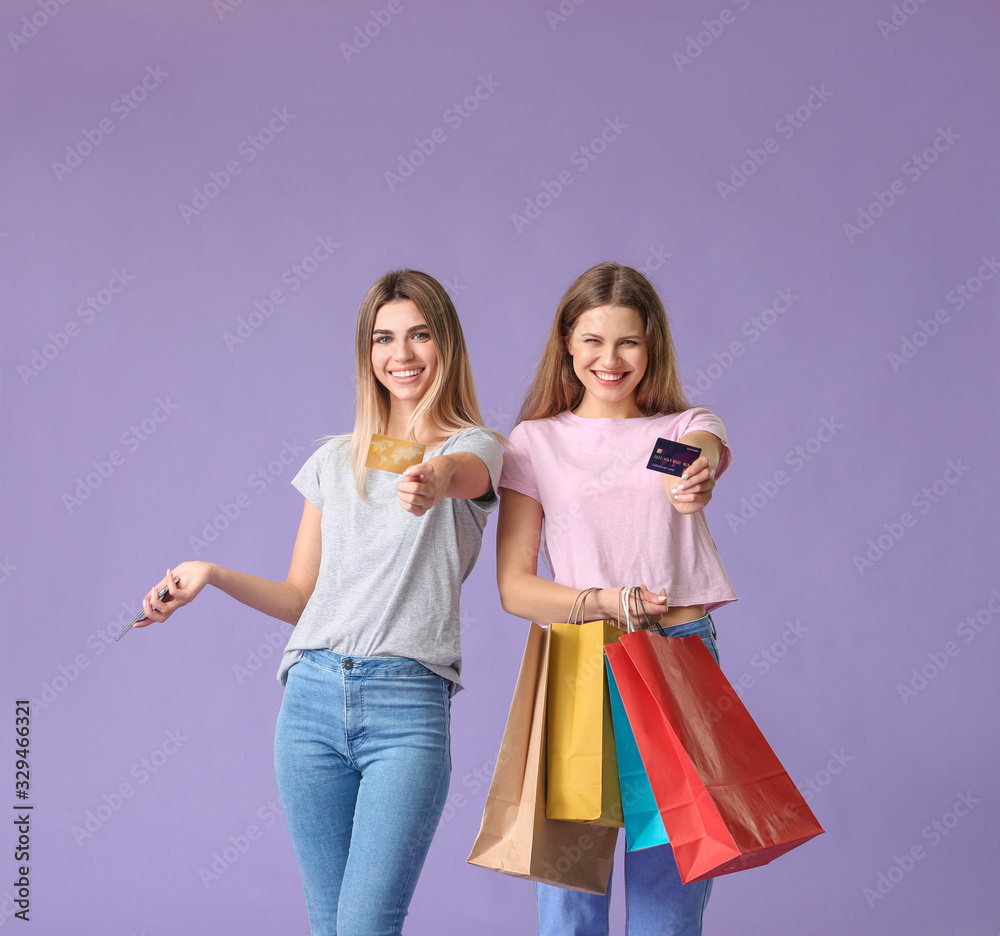 Young women with credit cards and shopping bags on color background