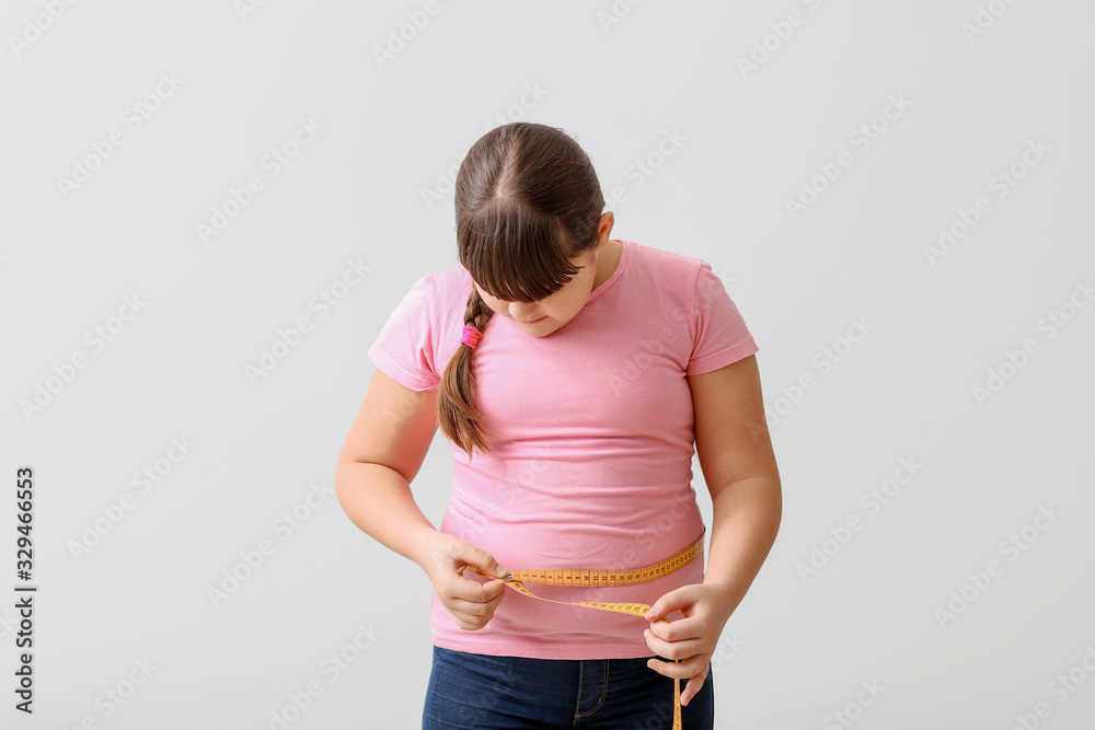 Overweight girl measuring her waist on light background