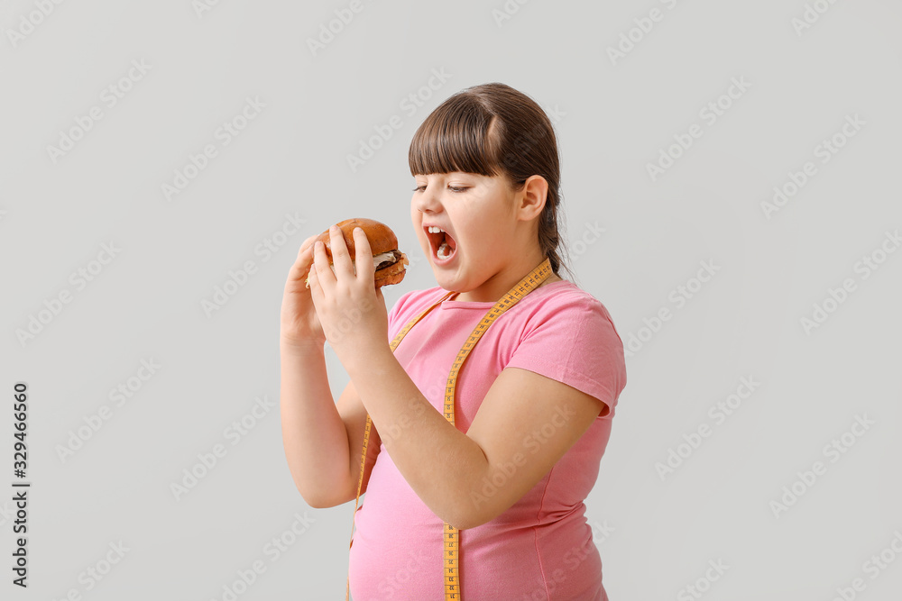 Overweight girl with unhealthy burger on light background