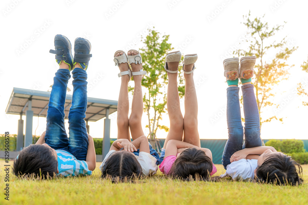 一大群快乐的亚洲微笑幼儿园的孩子朋友躺在草地上，把腿抬向天空