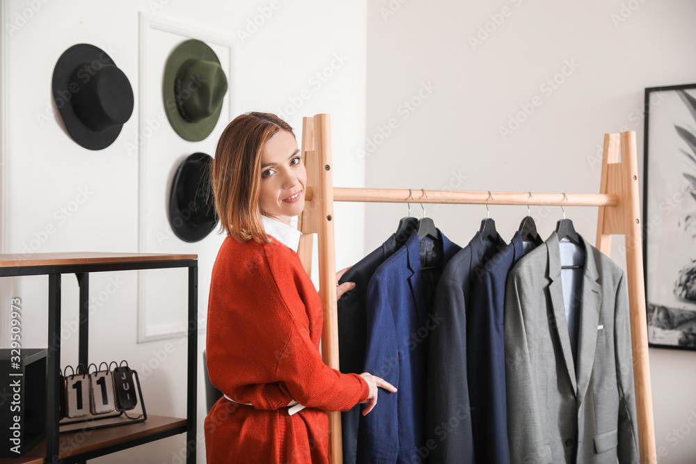 Female stylist near rack with male clothes in her studio