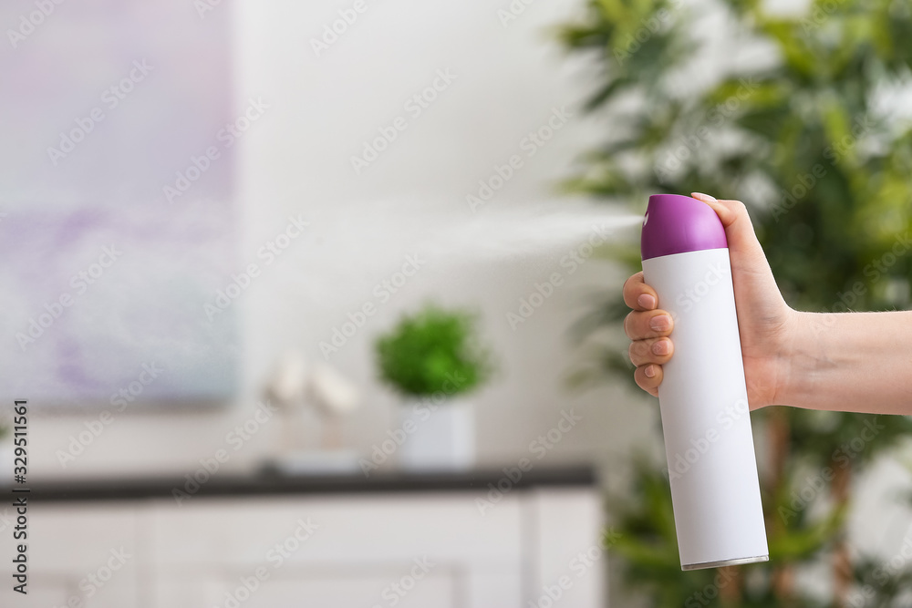 Woman spraying air freshener at home