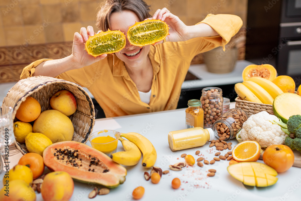 Portrait of a joyful woman with variety of exotic fruits and vegetables on the kitchen, holding slic