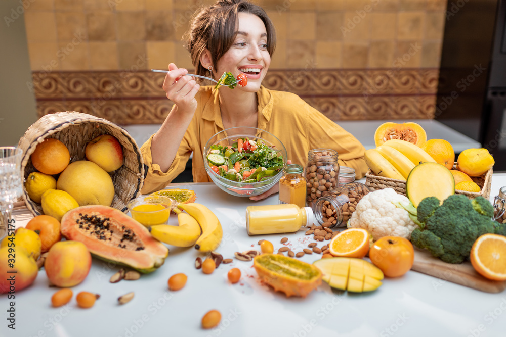 一个年轻快乐的女人在餐桌上吃沙拉的画像，餐桌上摆满了健康的生蔬菜和油炸食品