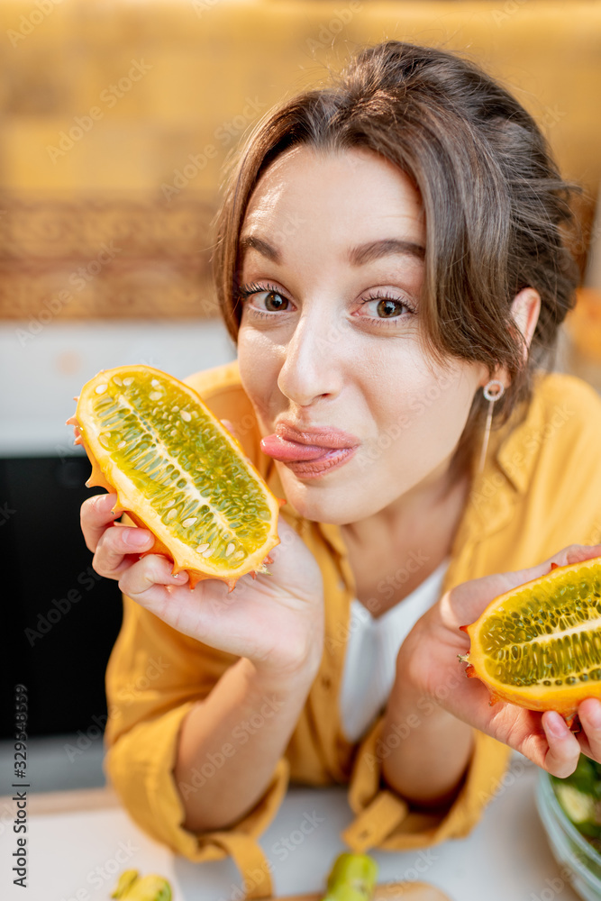 一个快乐的女人的画像，厨房里有各种各样的异国水果和蔬菜，手里拿着切片