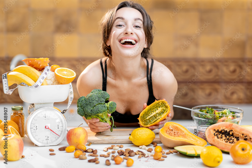 Portrait of a joyful sports woman with lots of healthy fresh food on the kitchen. Concept of losing 