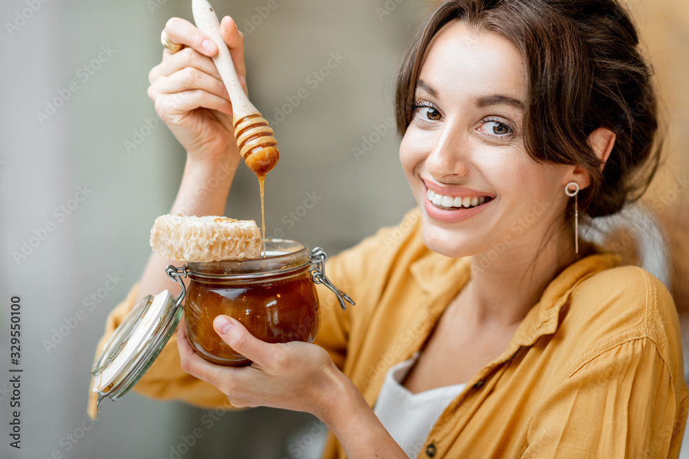 Portrait of a young and cheerful woman with a jar full of sweet honey on the kitchen at home