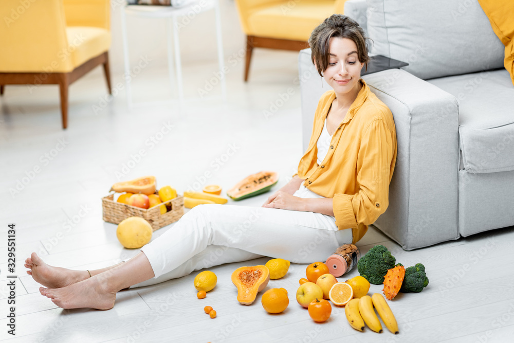 Portrait of a young and cheerful woman sitting with lots of fresh fruits and vegetables on the floor