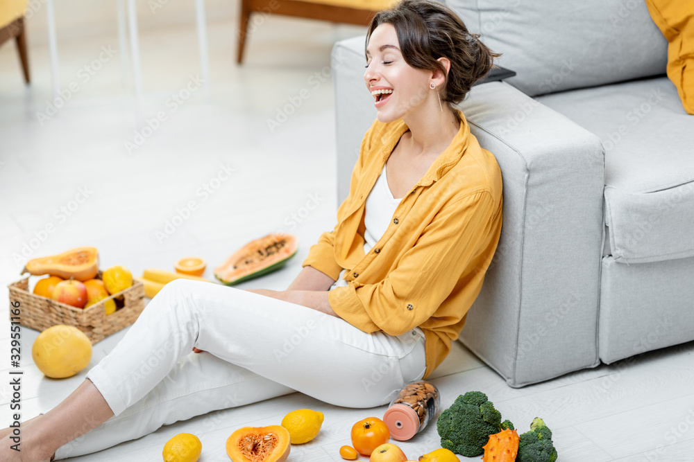 一个年轻开朗的女人坐在地板上，手里拿着很多新鲜水果和蔬菜的画像