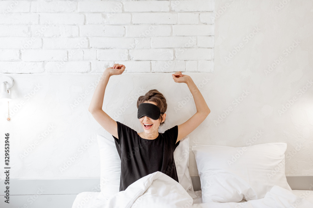 Young woman in sleeping mask waking up in the bedroom. Good morning concept