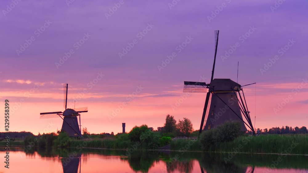 Holland windmills on the riverside at sunset; beautiful rural landscape at sunset