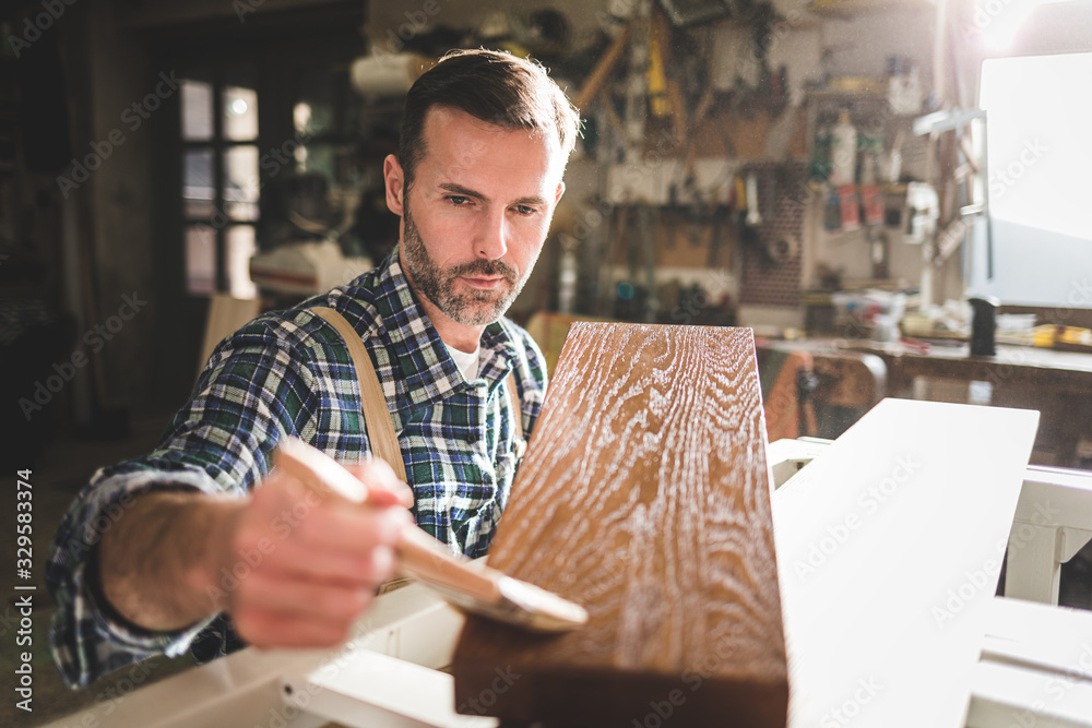 Craftsman painting a wooden board by paintbrush in his carpentry workshop