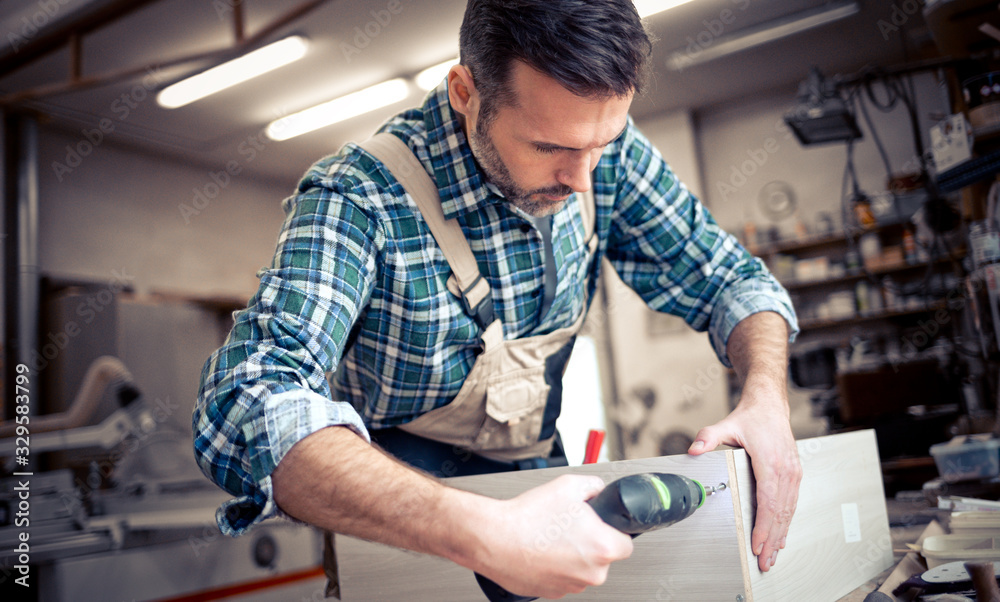 Craftsman drilling a hole by drill in a wooden board