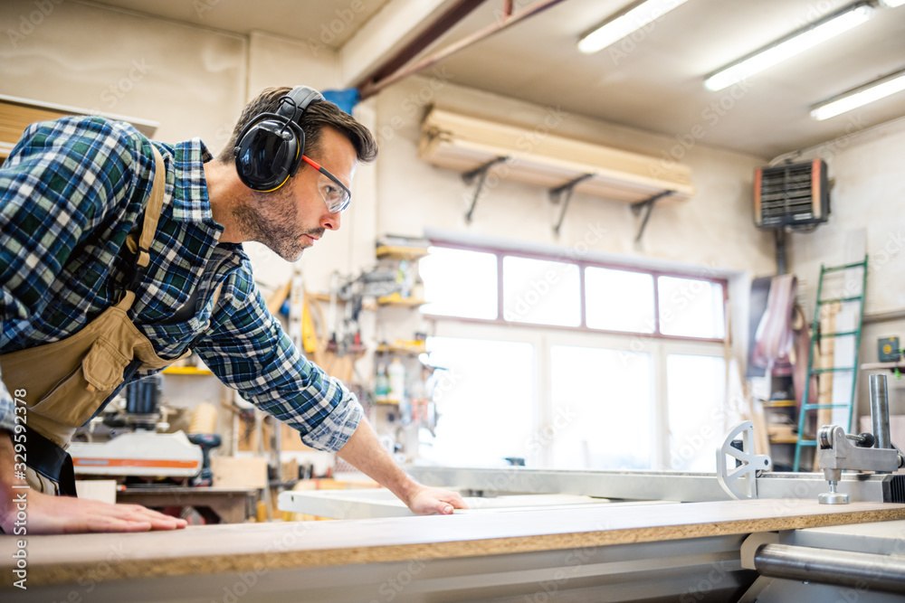 Carpenter using circular saw to cut a large wooden board at carpentry workshop