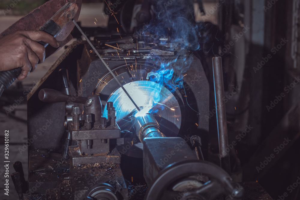 Close-up Profesional welder in safety protective uniform and mask welding metal pipe on the industri