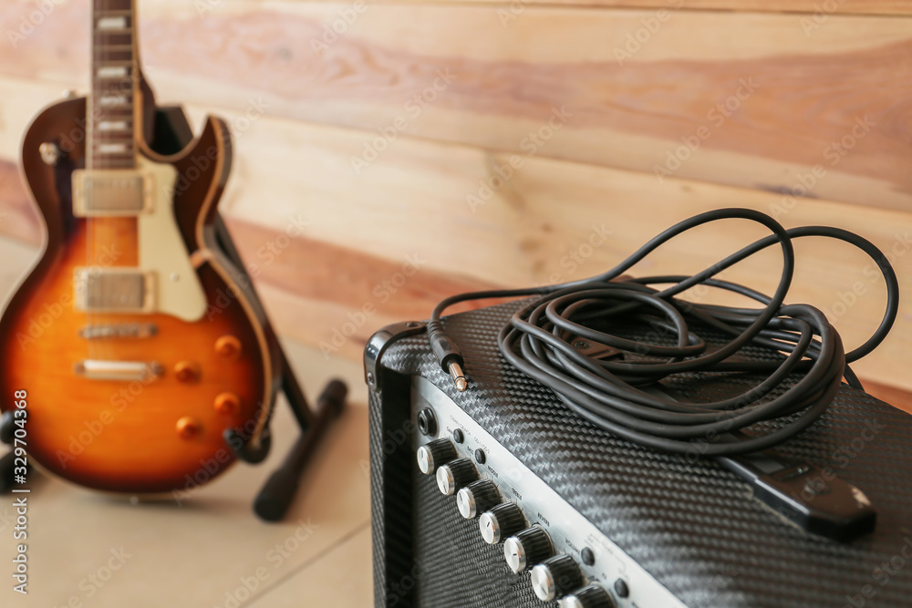 Modern amplifier and guitar near wooden wall, closeup