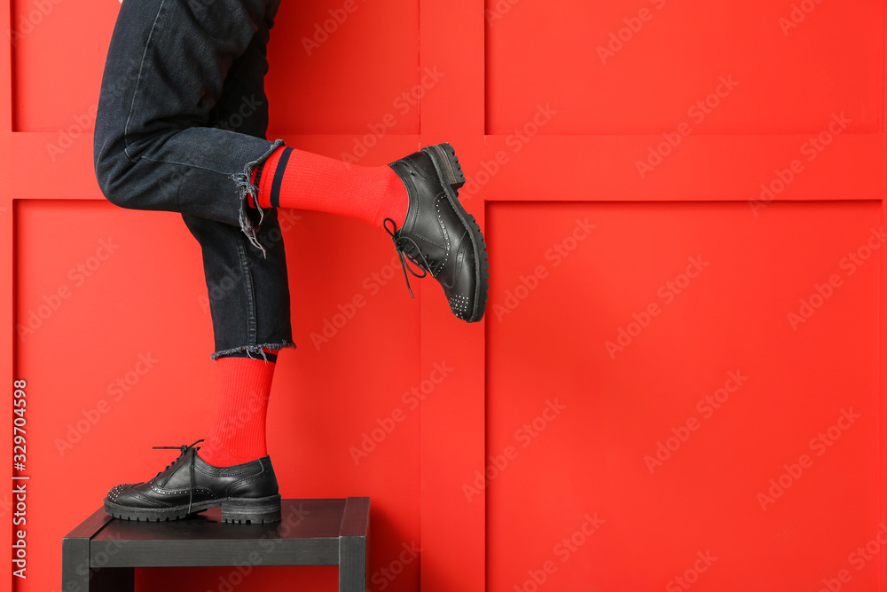 Legs of young woman in socks, shoes and jeans on color background