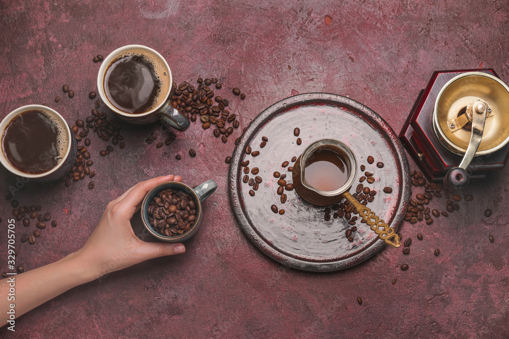 Female hand, cups of different coffee, jezve and grinder on color background