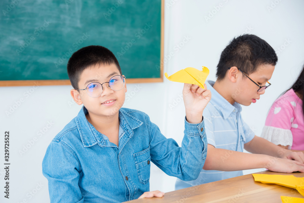 年轻的亚洲男孩在教室里玩纸飞机。