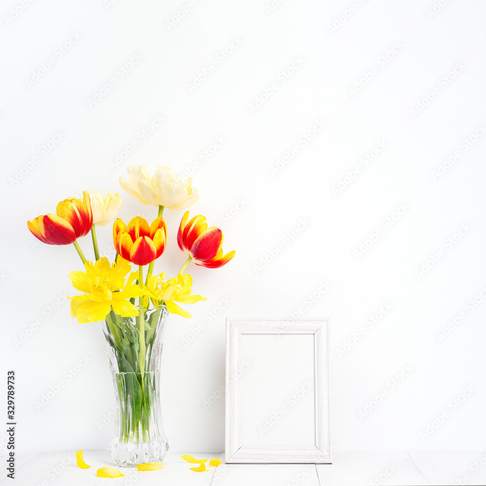 Tulip flower in glass vase with picture frame place on white wooden table background against clean w