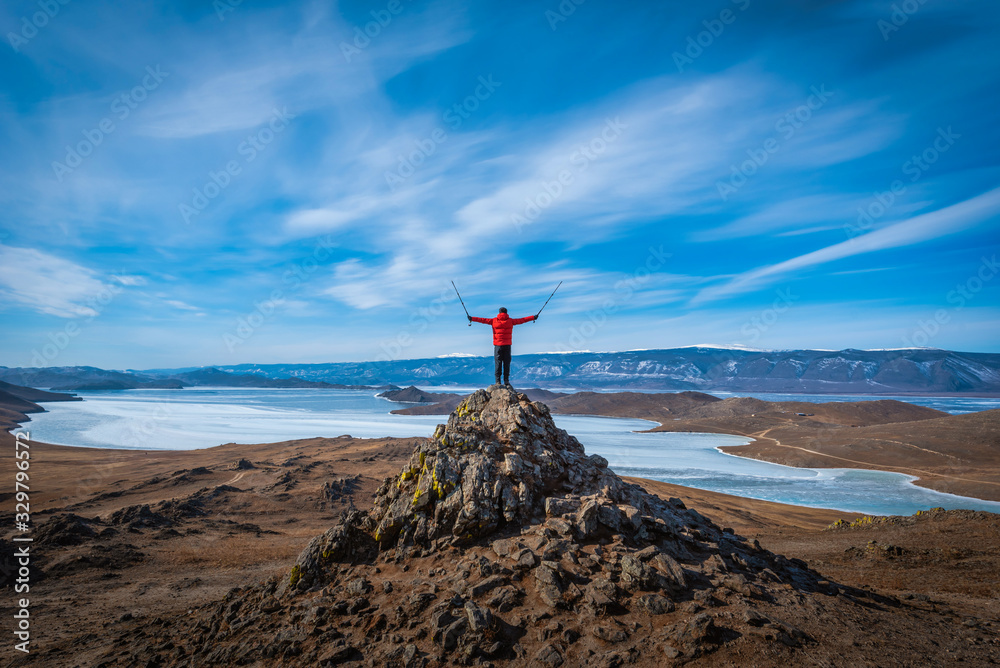 Traveler man wear red clothes and raising arm standing on mountain at daytime in Lake Baikal, Siberi