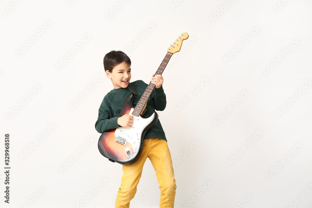 Little boy playing guitar on light background