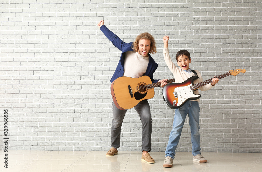 Emotional man and his little son playing guitars against brick wall