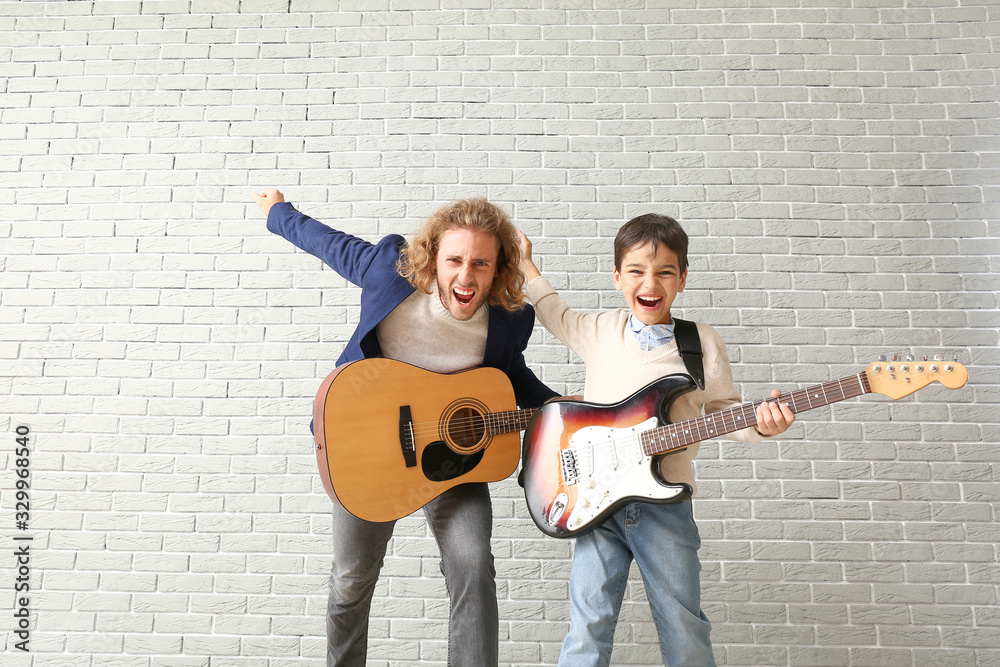 Emotional man and his little son playing guitars against brick wall