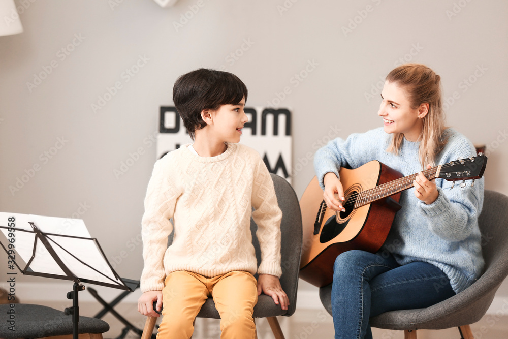 Private music teacher giving guitar lessons to little boy at home