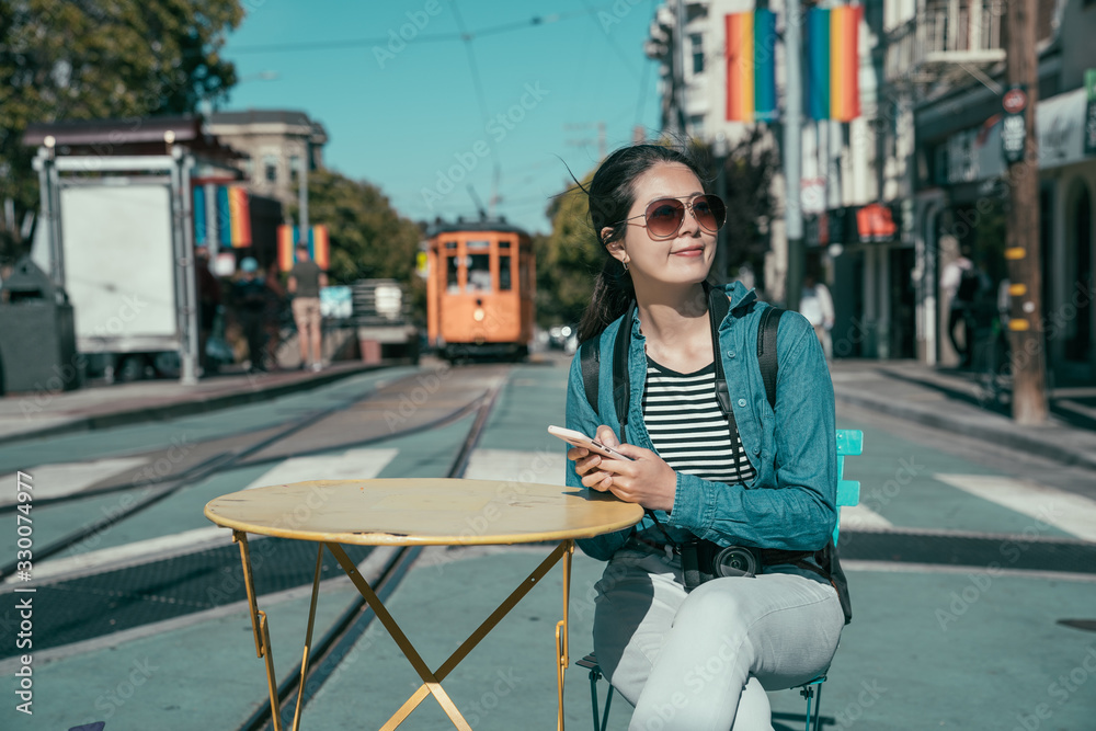 bokeh view of rainbow flags hanging on Castro street. smiling asian woman tourist in sunglasses rela