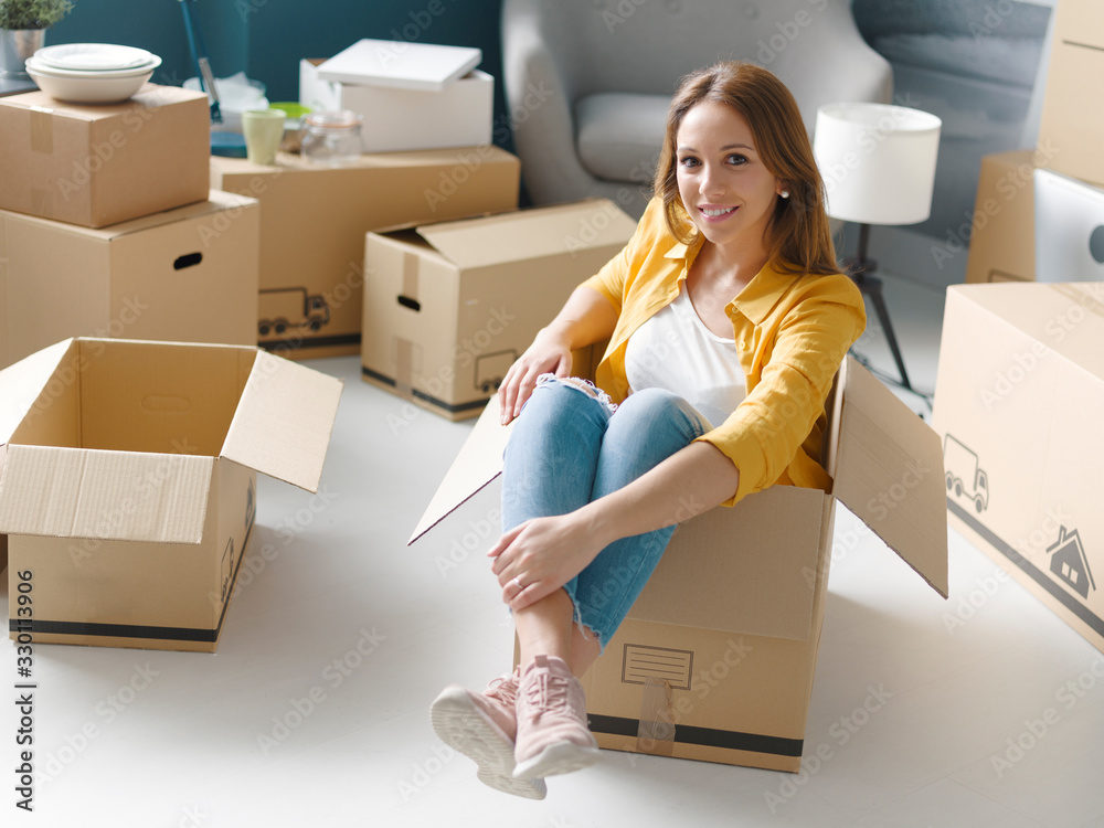 Smiling woman sitting in a cardboard boxing during relocation