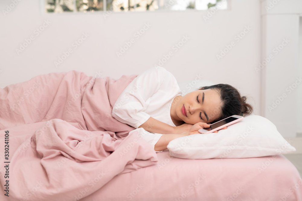 Photo of young asian woman sleeping with smartphone while lying on white pillow