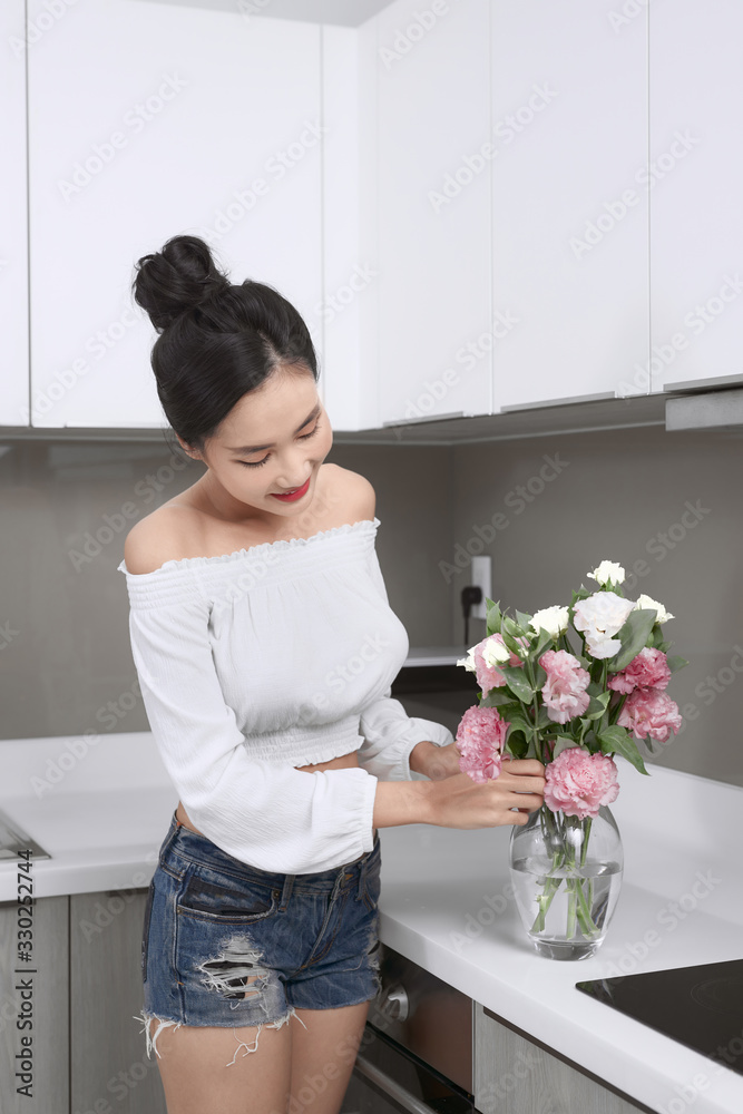 Young beautiful Asian woman arranging flowers in vase in kitchen.